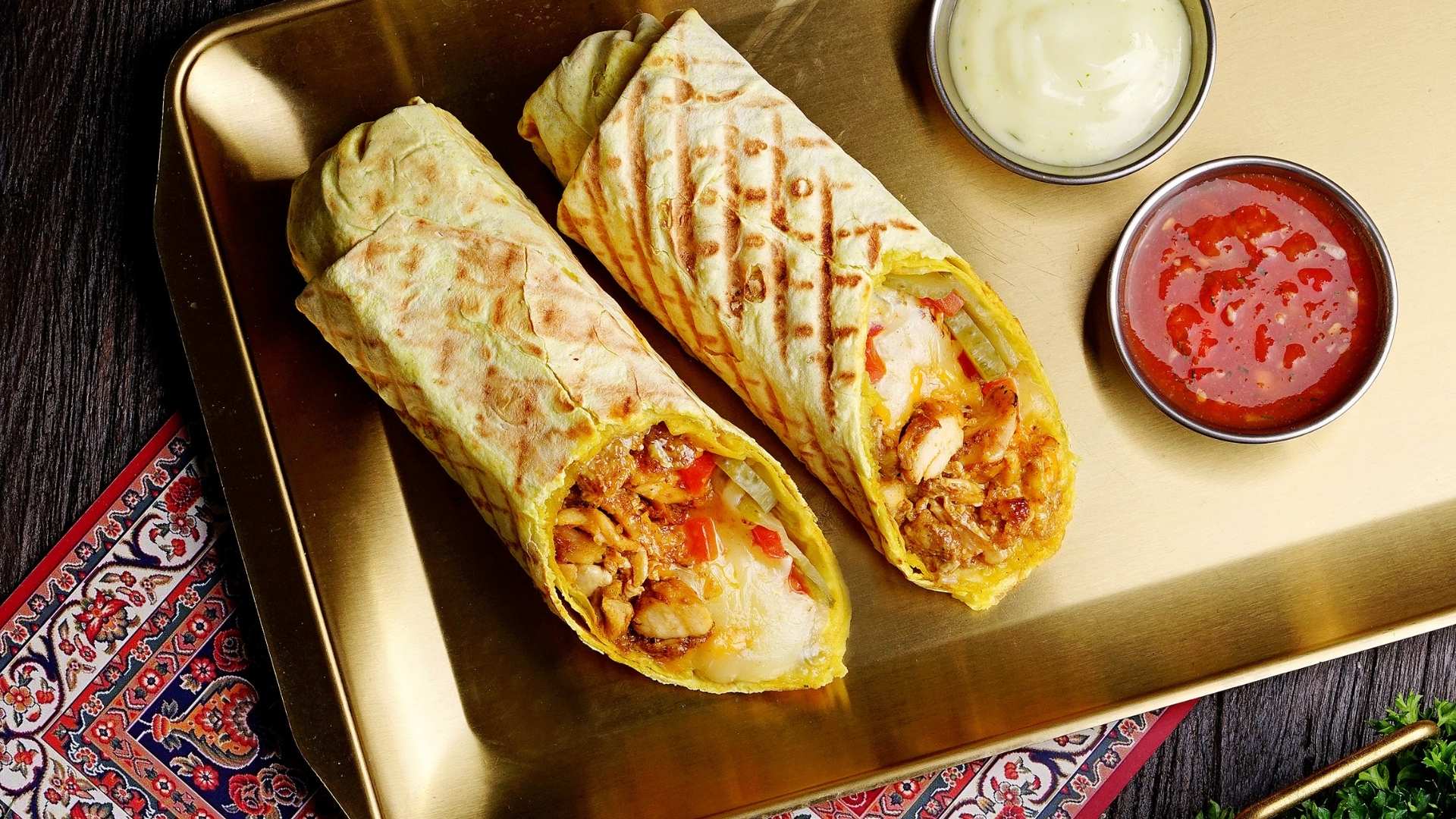 Two freshly grilled NENA shawarmas on a gold tray with sauces